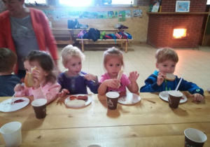 Dzieci jedzą kiełbaski z ogniska.