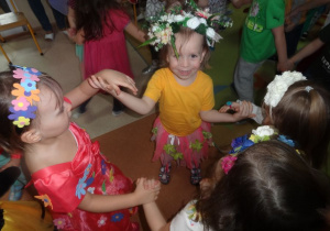 Dziewczynki w strojach wiosennych tańczą w kółeczku.