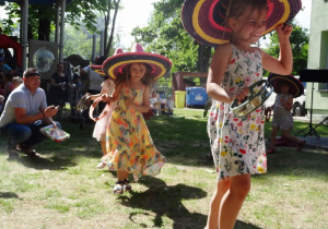 Dziewczynki w kapeluszach z tamburynem tańczą.