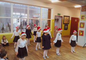 Dziewczynki w czapkach mikołaja tańczą taniec.