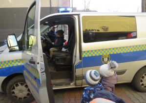 Dzieci siedzą w samochodzie straży miejskiej.